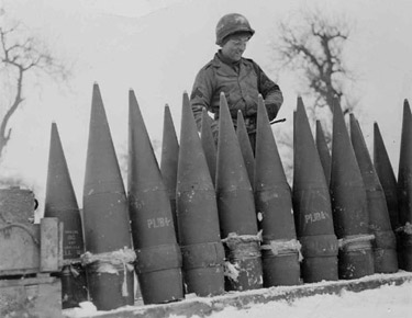 Photograph of soldier standing next to 8-inch gun ammunition for the 243rd Field Artillery